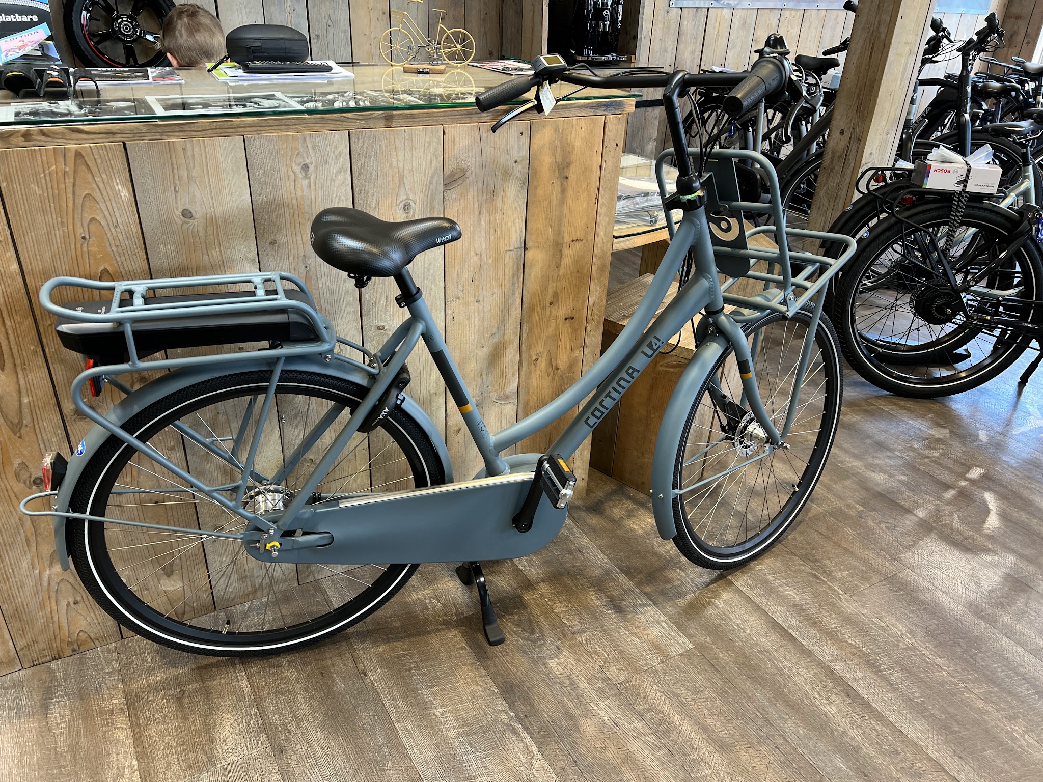 Een grijze transportfiets bij de houten toonbank